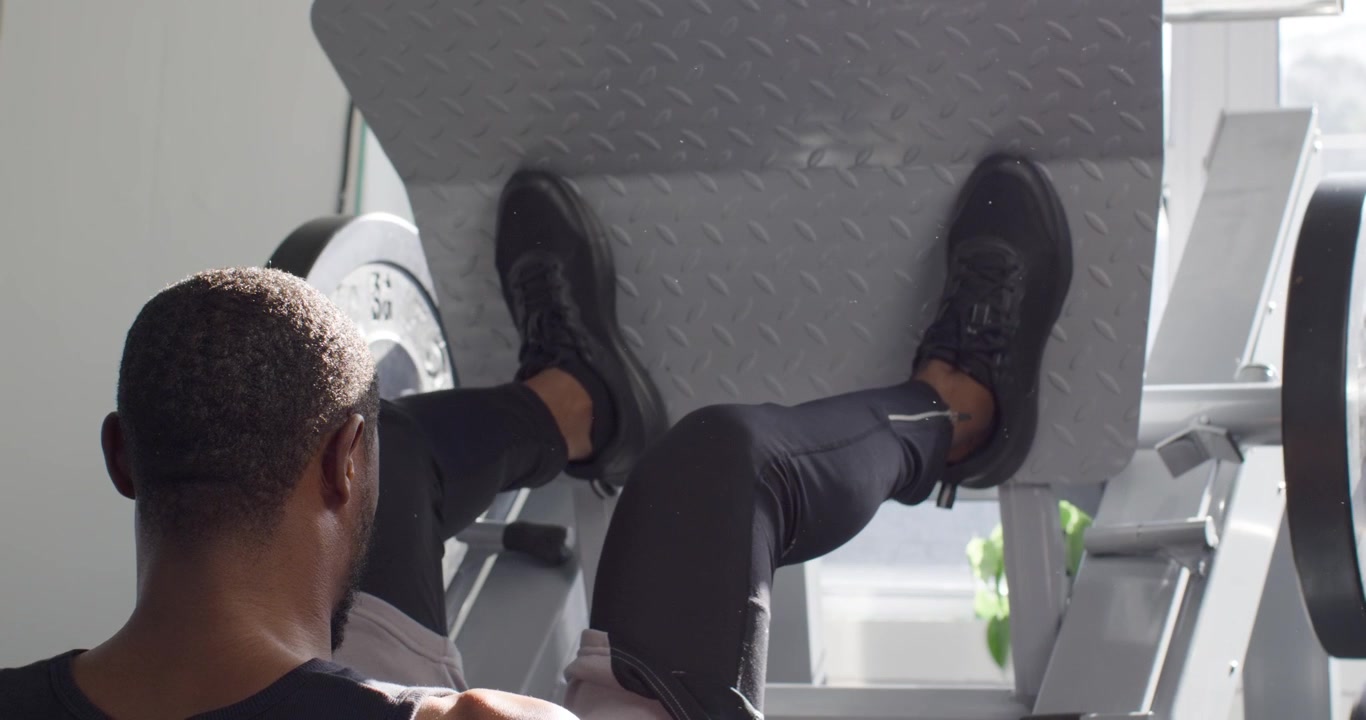 Man in workout top performing leg presses from feet planted on platform at gym for strength