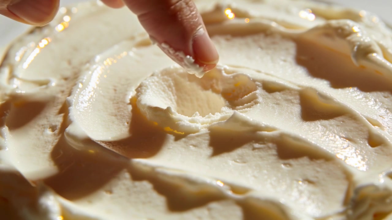 Pressing adult fingertip creating round indentation in shallow dish, revealing glossy syrup beneath