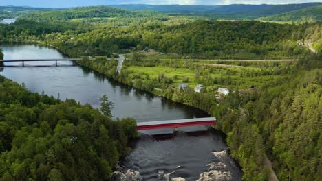 Dolly-Aéreo-Hacia-Atrás-Panorámica-Para-Revelar-Un-Puente-Cubierto-Ubicado-En-Un-Valle-Fluvial-En-Un-Paisaje-Verde-Montañoso-En-Wakefield-Quebec-Canadá