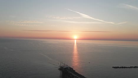 Aerial-seascape-panoramic-view-of-a-trabucco-silhouette,-a-traditional-fishing-machine,-on-the-italian-coastline,-at-sunset