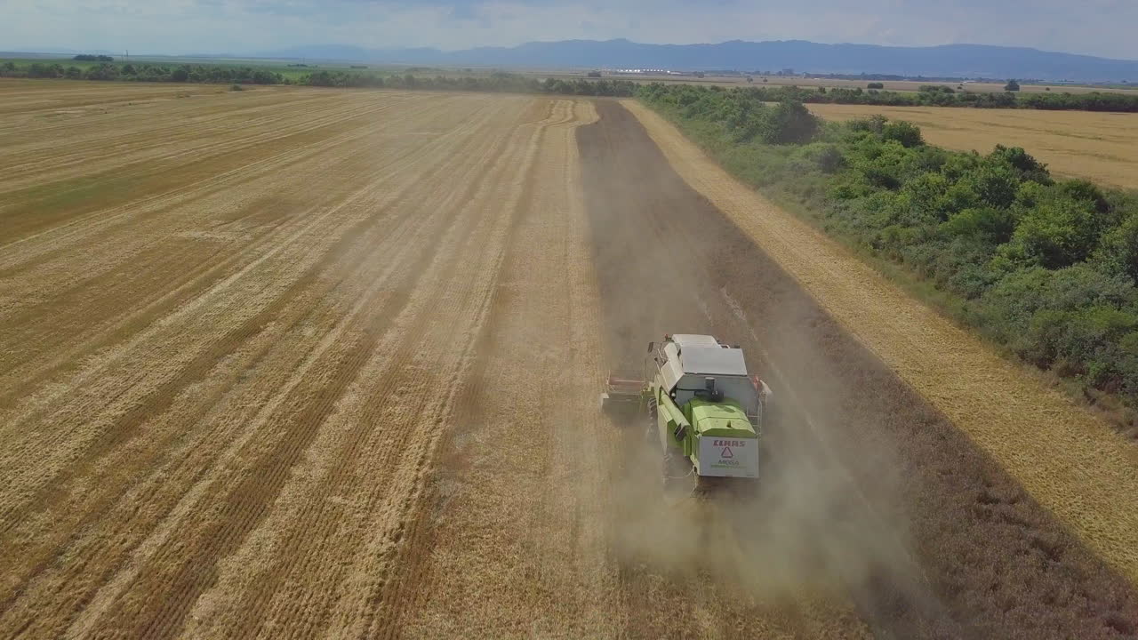 Drone shot over reaping harvester in agriculture field