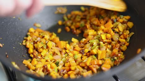 cooking and stirring chopped vegetables in pan with wooden spoon