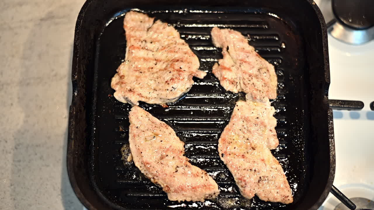 Savory chicken fillets are sizzling on a grill pan in a warm kitchen. Watch as they turn golden brown, releasing delicious aromas of spices and herbs