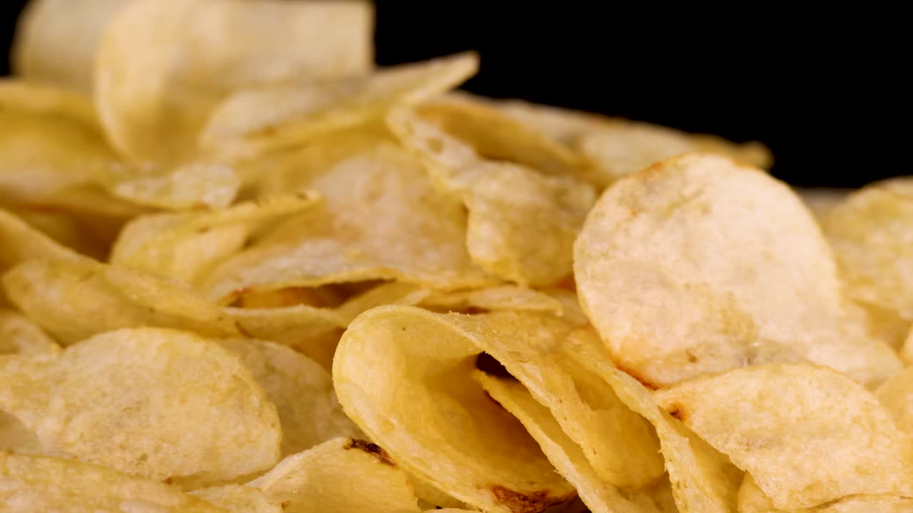 Golden potato chips rotate slowly under studio lighting, highlighting texture and crispness on black background