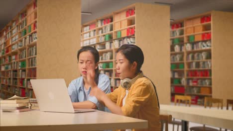 asian woman students arguing about something on the laptop while sitting on a table studying in the library