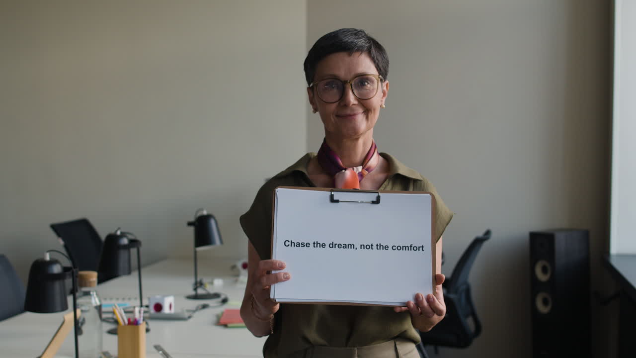 Woman in an office holding a motivational sign with the text "Chase the dream, not the comfort"