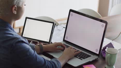 mujer biracial ocupada trabajando en casa con computadora portátil y tableta con espacio de copia en cámara lenta