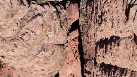 Drone-flying-over-red-rock-desert,-looking-down-over-slot-canyon