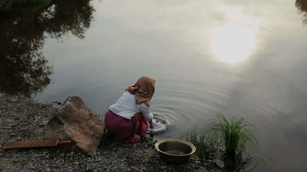 Woman Washing Clothes by a River at Sunset