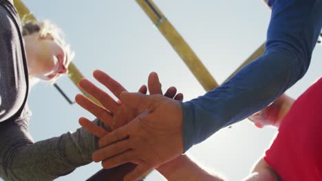 happy, fit diverse group making hand stack and cheering in the sun after obstacle course