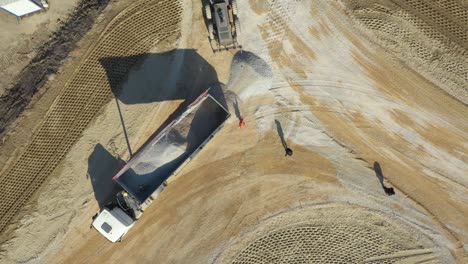 aerial view on tipper truck is unloading gravel from trailer over construction site for new traffic roundabout