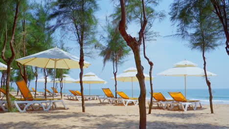 playa tropical de arena natural y olas marinas con un banco de playa amarillo bajo una sombrilla blanca y árboles en la playa de una isla tropical