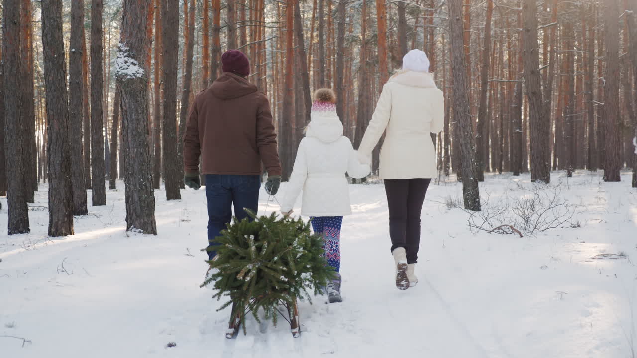 아이를 안고 있는 부부가 눈 덮인 숲을 걷고 있다 소녀가 썰매를 끌고 있다