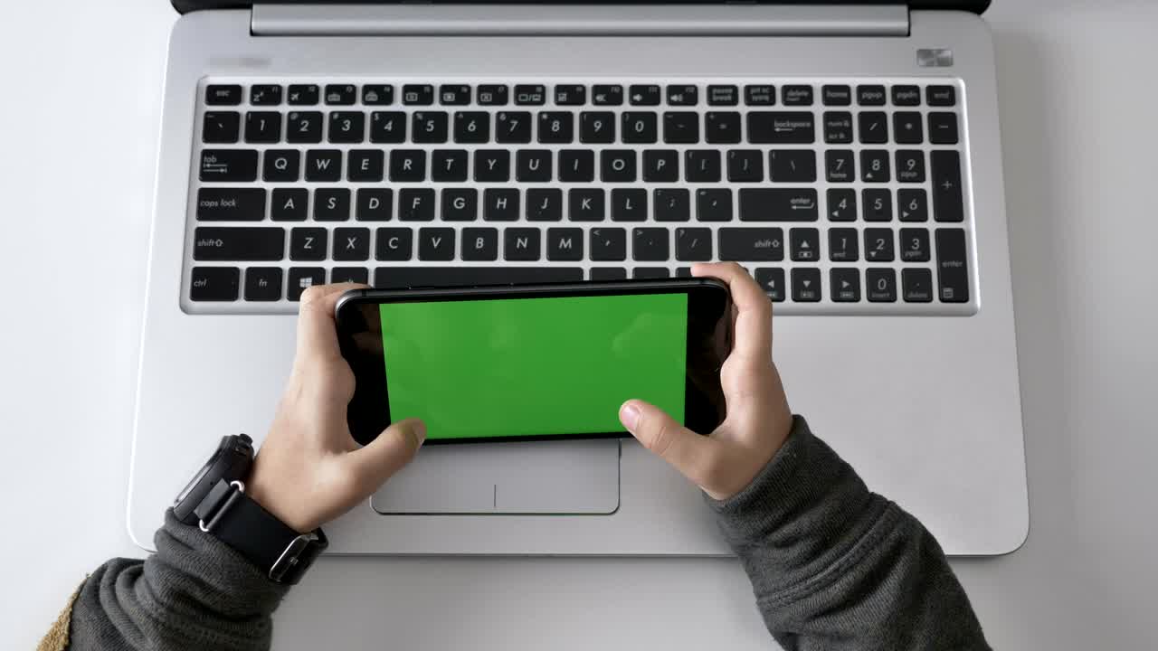 Children's hands playing on a smartphone, Green screen, chromakey concept, laptop in the background. Top shot 60 fps