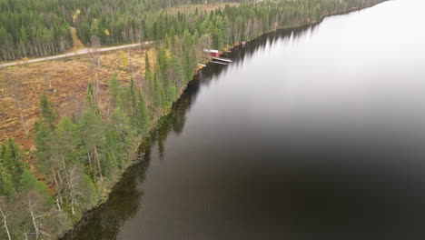 Sweden---Enchanting-Lake-Encircled-by-Fir-and-Birch-Forests-Adorned-with-Autumnal-Hues,-Casting-Reflections-on-the-Tranquil-Water-During-a-Cloudy-October-Day---Aerial-Pullback