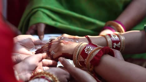 mujeres indias vestidas con atuendos vibrantes y coloridos haciendo un ritual de boda tradicional bengalí con manos de henna y leche