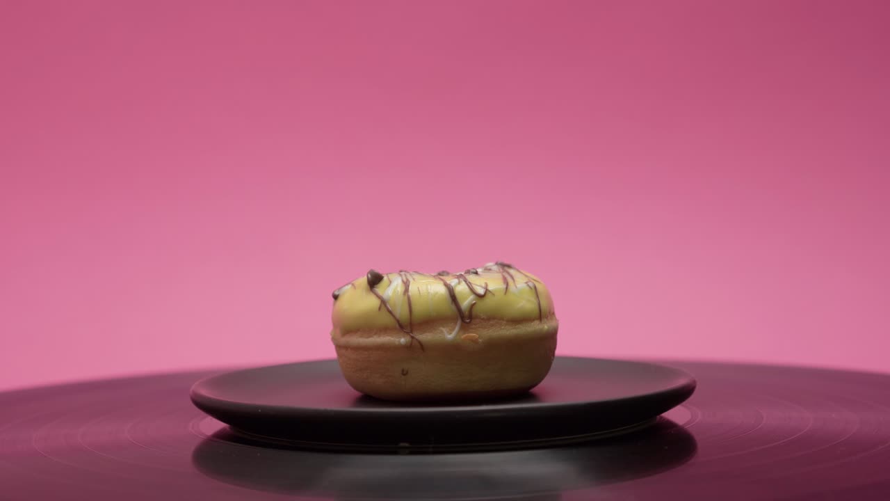 Delicious american donut with yellow chocolate and black chocolate spin in a circle on a pink and a black background