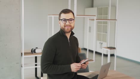 a charming, cheerful, and charismatic man with a tablet shifts his gaze to the camera and begins to smile