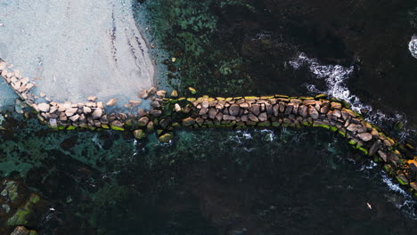 Möwen-Schweben-Entlang-Der-Mole,-Die-Aus-Einem-Grauweißen-Strand-Gebaut-Wurde,-Drohnenansicht