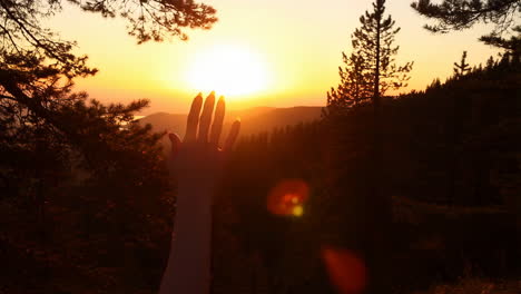 hand reaching towards a golden sunset over mountains