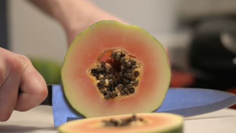 narrow focus close-up: slicing ripe orange papaya fruit with seeds