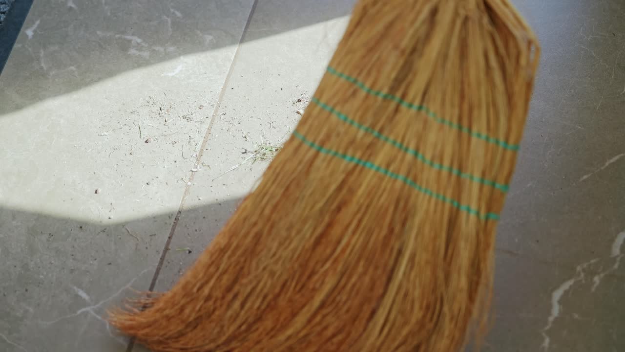 Slow motion sweeping on tiled floor with broom in countryside house, sunny day
