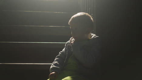 sad child silhouette on stairs at night. boy waits on steps while parents quarrel in cottage house. kid sits alone on staircase steps of rural home