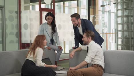 a business working group consisting of two women and two men have a relaxed meeting in the armchairs in the common area of the offices 1