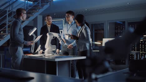 team of electronics development engineers standing at the desk working on robot arm prototype. specialists working on ultra modern industrial design, using tablet computer, laptop. in slow motion