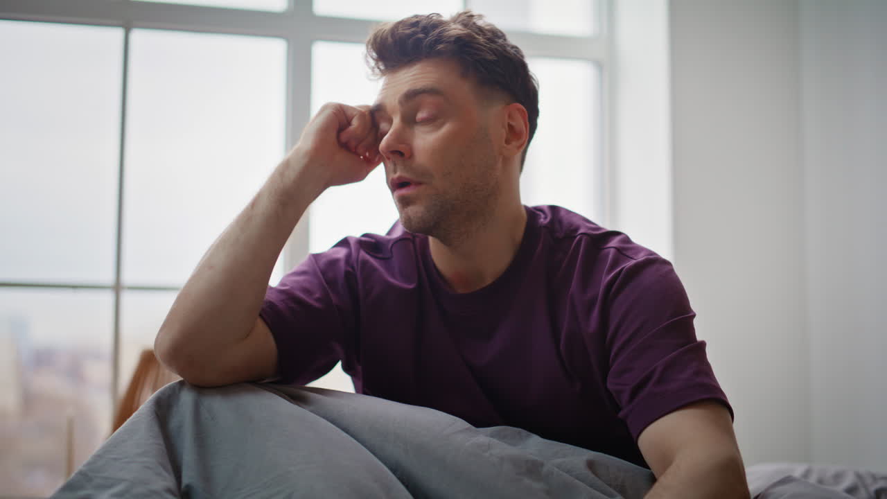 Uomo con i postumi della sbornia che ha mal di testa e tossisce, soffre al risveglio sul letto, primo piano.