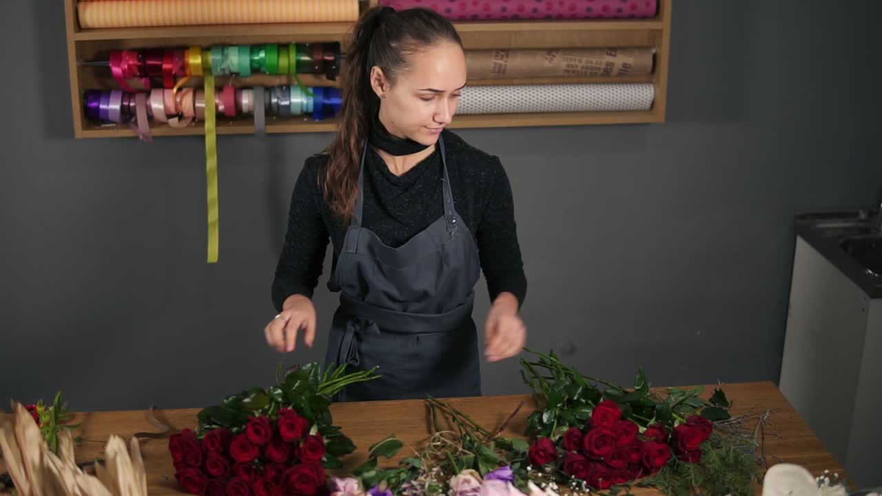 Giovane fiorista donna che compone un bouquet moderno usando bellissime rose rosse in un negozio di fiori. Riprese al rallentatore.