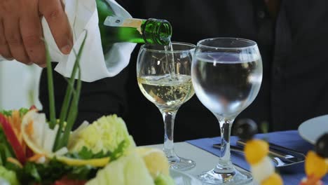 the waiter pours white wine in wine glass in the restaurant