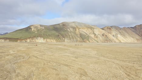 landmannalaugar mountains and fields with tourists riding horses in iceland - drone shot