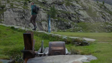 Male-hiker-walks-behind-ancient-watermill-in-mountains