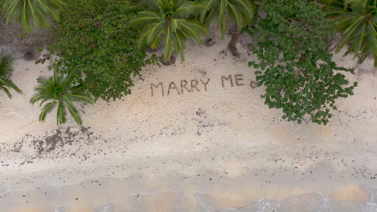 Marry Me' written in the sand on a tropical beach