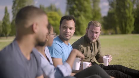 cheerful friends sitting in row on lawn and communicating