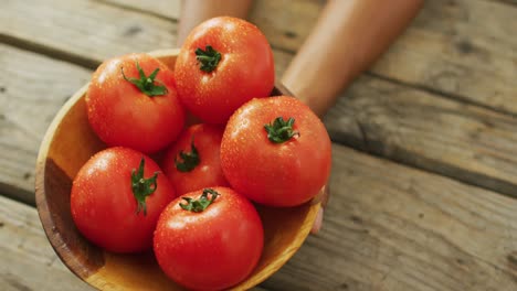 Video-of-biracial-man-holding-bowl-of-fresh-red-tomatoes-on-wooden-background