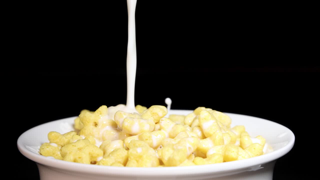 Milk cascades into a bowl of star-shaped cereal against a black background, creating a dynamic breakfast scene