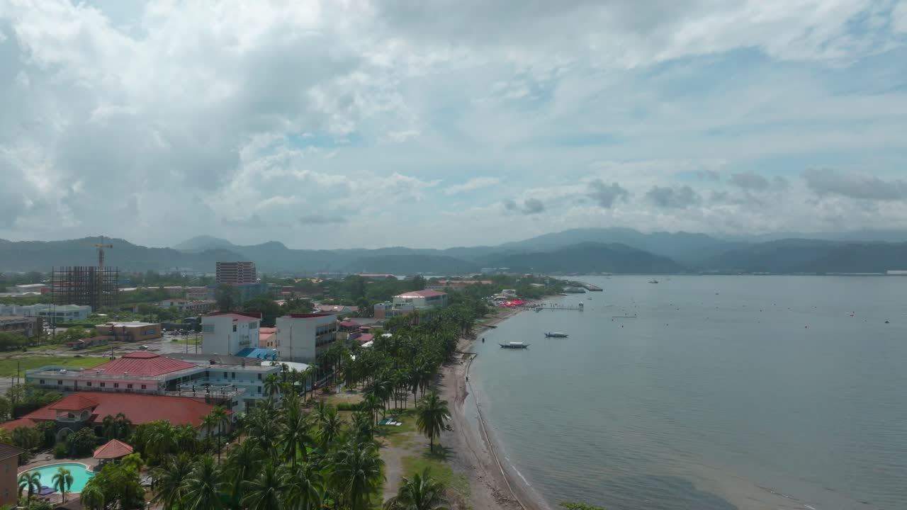 A breathtaking drone shot showcases the scenic shoreline, with a towering lighthouse, clear blue skies, and coastal buildings lining the view.