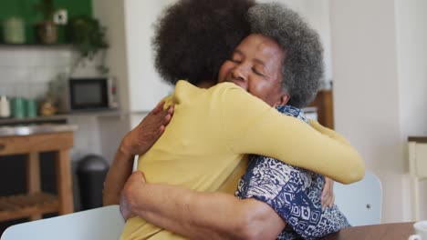 happy african american adult daughter and senior mother hugging in kitchen at home, slow motion