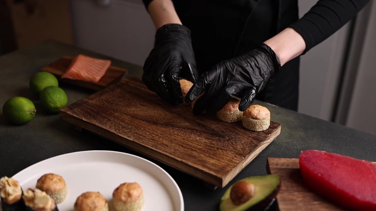 Chef de Luvas Pretas Organizando Rolos de Sushi em Tábua de Madeira