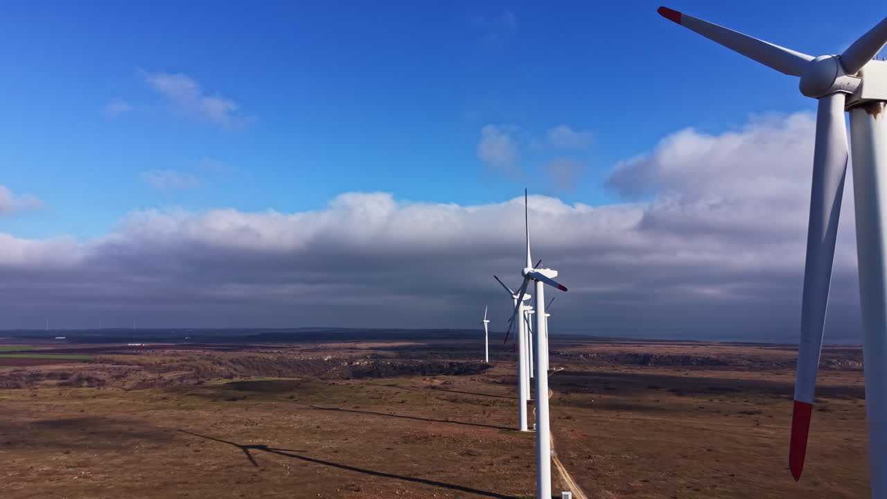Vista di turbine eoliche in un campo sotto un cielo azzurro terso con alcune nuvole, che mostra la produzione di energia pulita e gli sforzi ambientali in una zona rurale durante il giorno