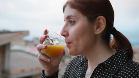 woman drinks orange carrot juice to take vitamins in the morning on the balcony