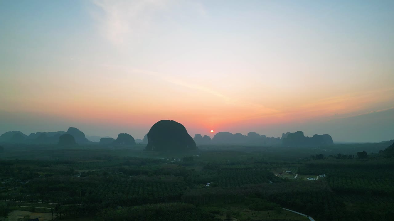 Aerial view of the sun rising over misty limestone mountains and lush farmland at Din Daeng Doi in southern Thailand