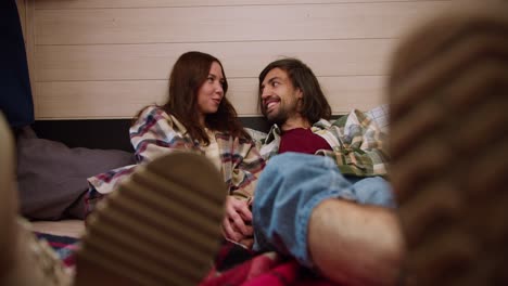 Close-up-shot-of-a-brunette-girl-in-a-plaid-shirt-lying-on-a-bed-in-a-trailer-with-her-brunette-boyfriend-and-they-put-their-legs-forward-touching.-Happy-couple-guy-and-girl-brunettes-in-plaid-shirts-relax-in-a-trailer-outside-the-city-during-a-picnic-at-a-camp-in-the-summer