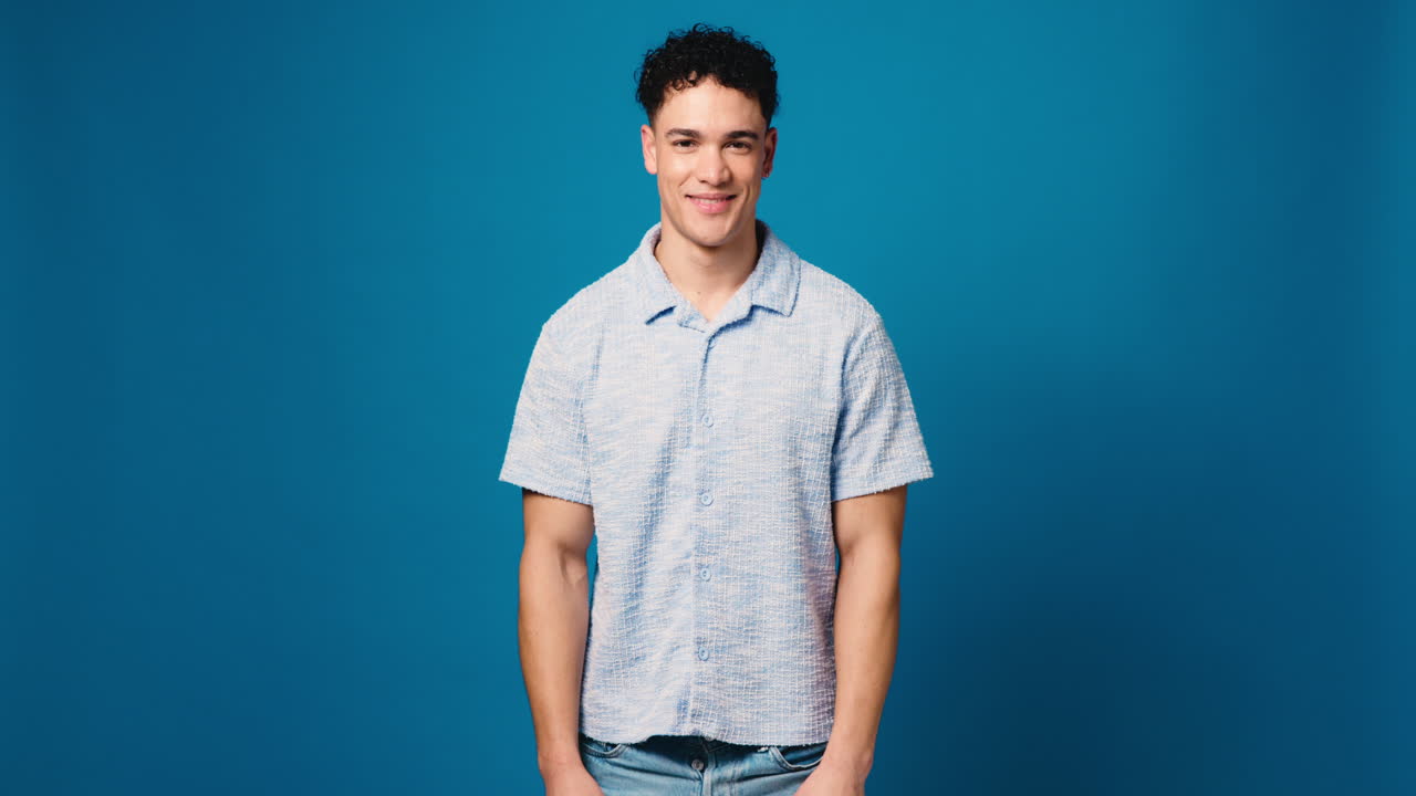 Portrait of a young man with curly hair smiling against a blue background