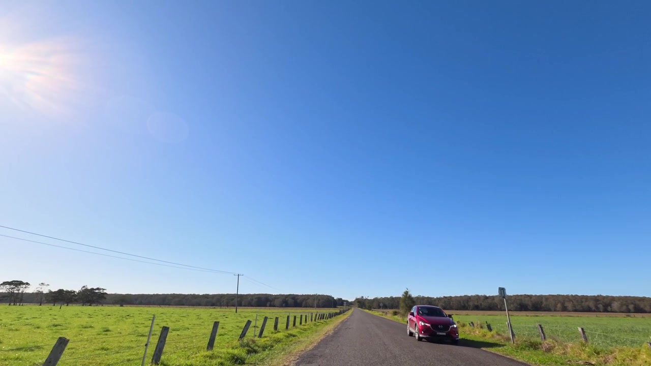 Wide point-of-view shot driving down a straight rural road under clear blue skies in Australia.