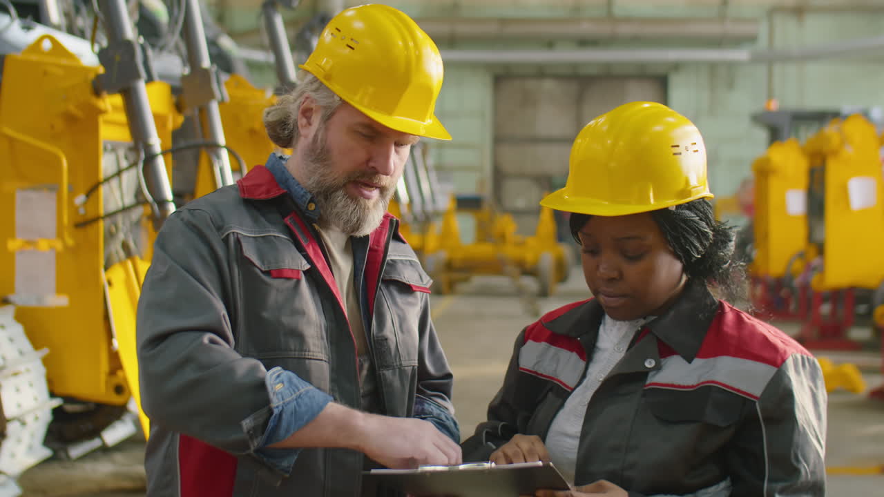 Colegas diversos de capacetes de segurança conversando no trabalho em uma fábrica de máquinas