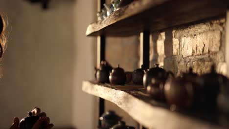 woman selecting a teapot from a collection on a wooden shelf