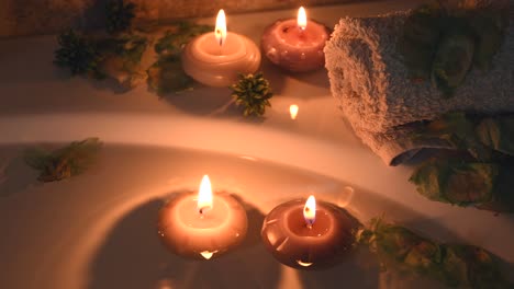 relaxing spa background with candles floating in the bath water, some green petals and a towel near the water surface